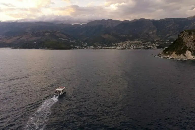 La baia di Himara al crepuscolo, con una barca e il paese sulla riva