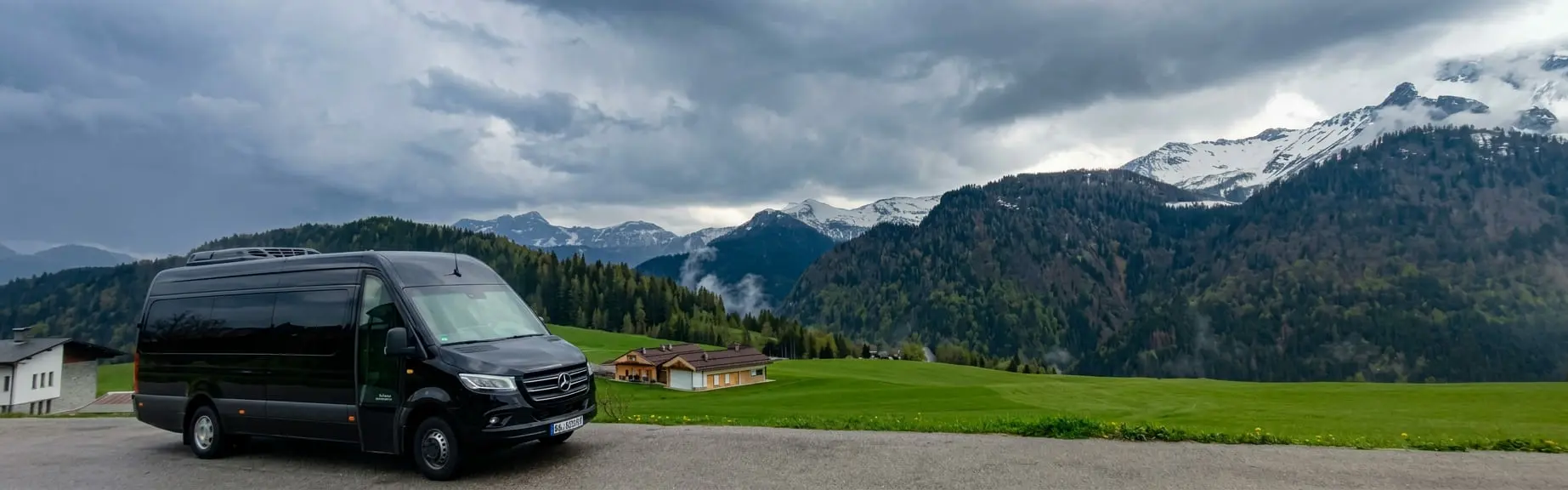 Minibus Mercedes-Benz Sprinter nero accanto a un verde prato di montagna con cime innevate